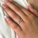 Woman wearing a gold opal ring with light-colored nail polish on a neutral background
