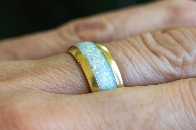 a person’s hand wearing a white opal wedding ring with a gold band